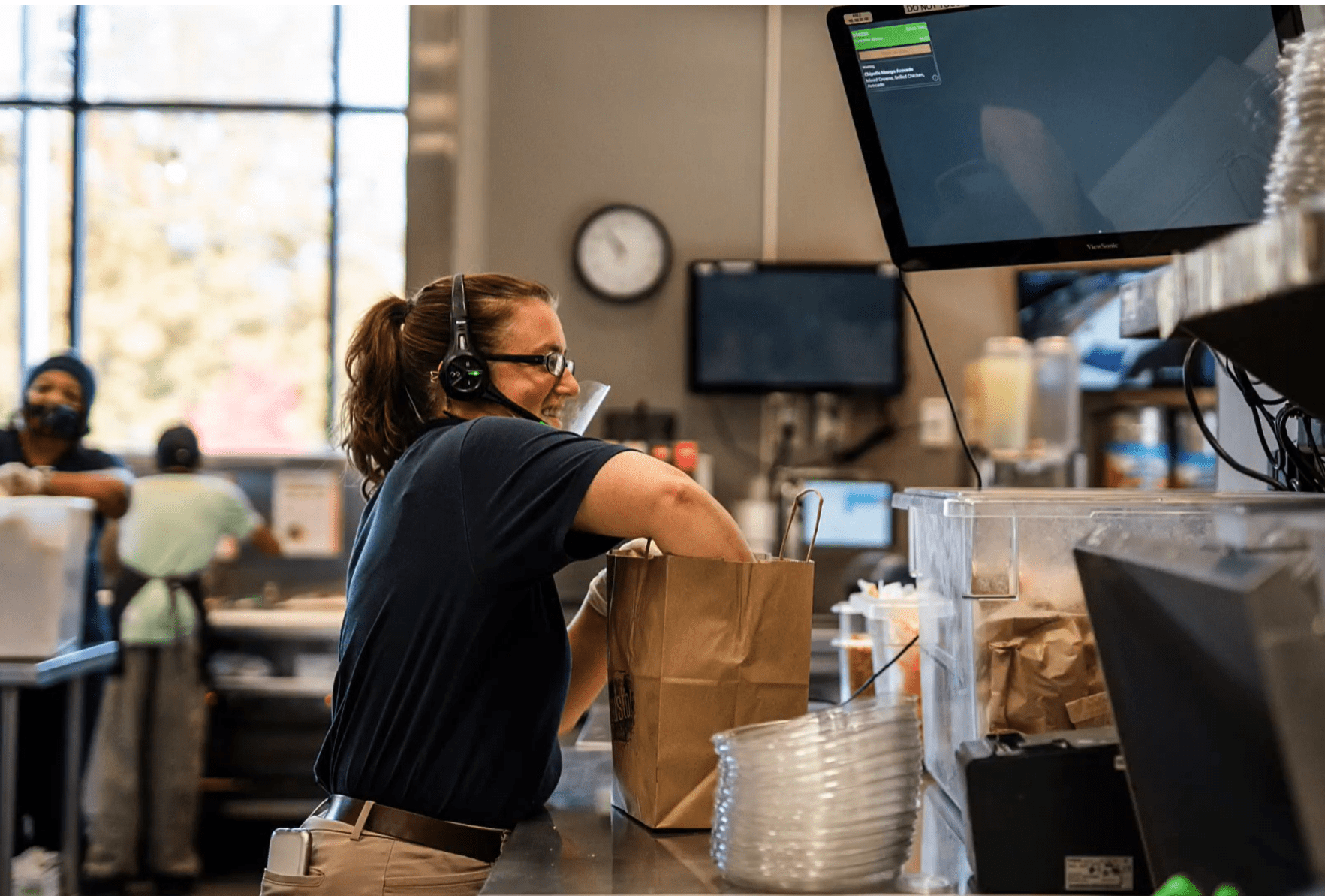 Kitchen staff taking a new drive-thru order while packing an order listed on the KDS screen